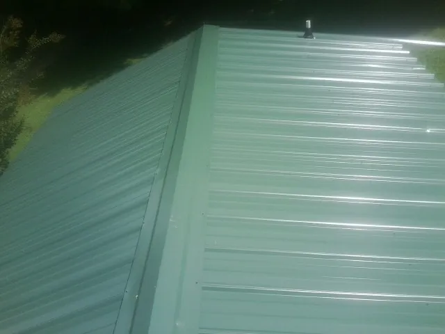 New green metal panels meeting at the ridge of a roof — Flat Roof Repair work by our crew in Defiance