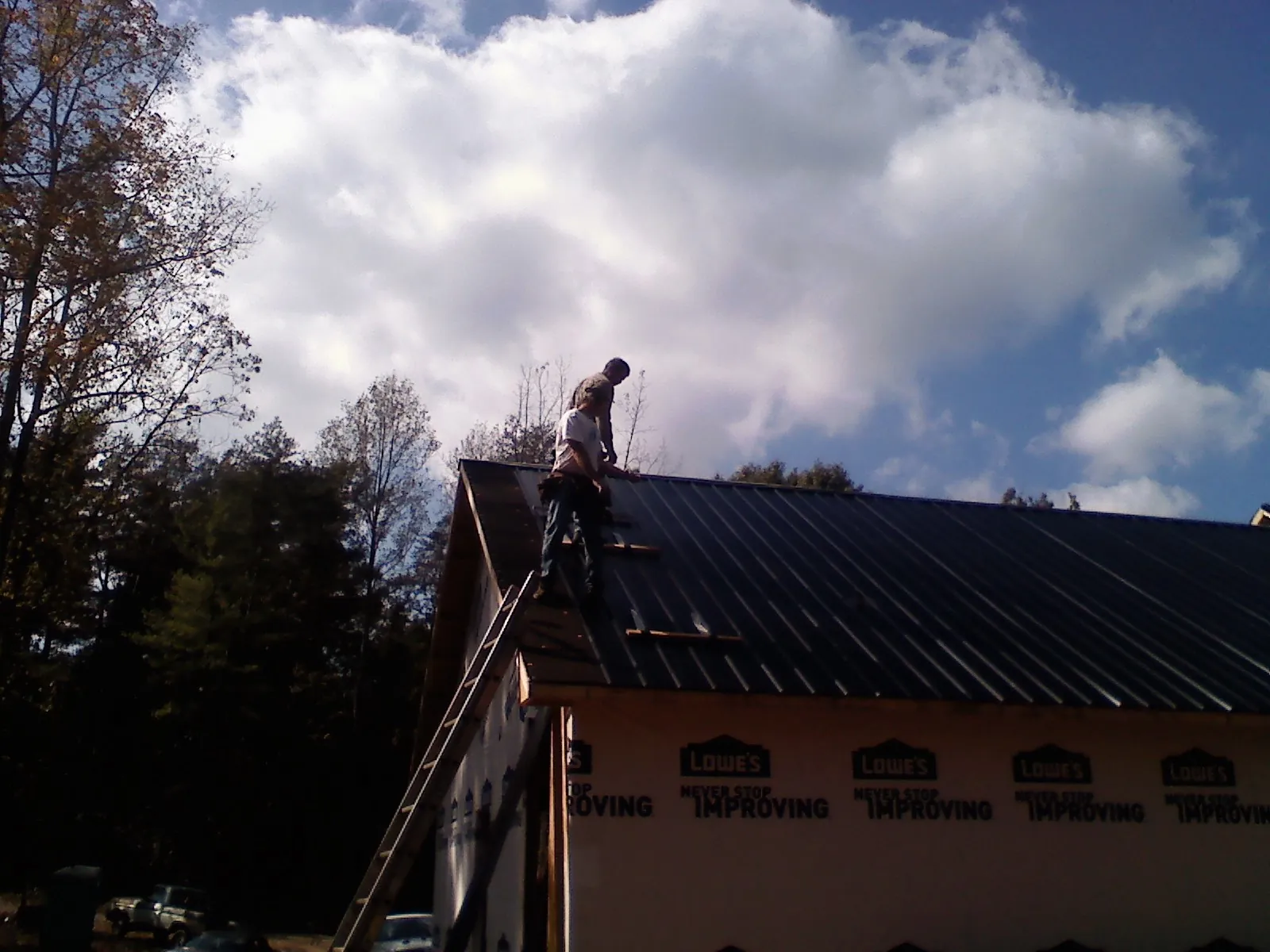 Roofer fastening dark metal panels high against a cloudy sky, from a Roof Inspection job in Defiance